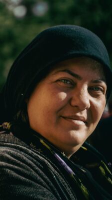 Close-up portrait of a woman smiling warmly outdoors in the sun.