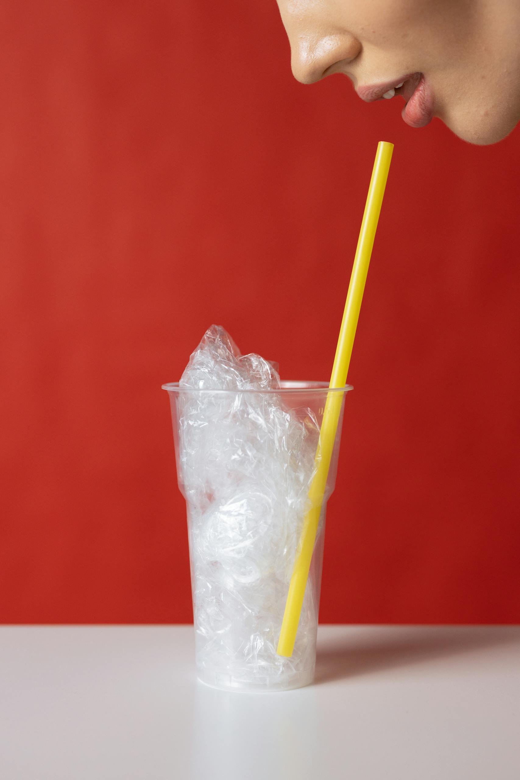 A woman sips from a plastic cup filled with plastic, highlighting pollution.